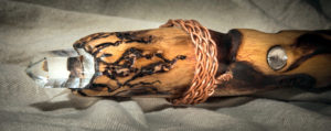A one foot tall, three-inch diameter section of an oak staff, burned with artistic representations of flames. The left side of the image is the top of the staff showing a clear quartz crystal embedded in the top. 3 inches down from the top, copper wire is braided around the staff. 3 inches below the braided copper is an inset Herkimer diamond.